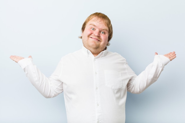 Young authentic redhead fat man makes scale with arms, feels happy and confident.