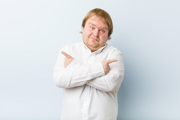 Young authentic redhead fat man points sideways, is trying to choose between two options.