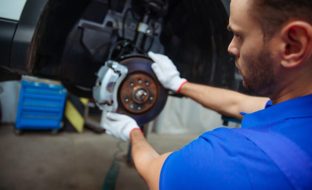 Photo young auto mechanic in a special suit repairs the brake system of a car or changes the brake pads