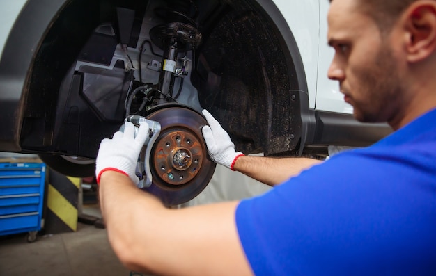 Young auto mechanic in a special suit repairs the brake system of a car or changes the brake pads