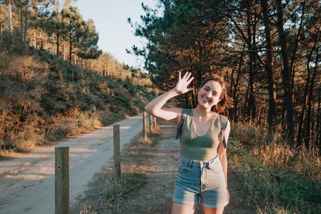 Young backpack girl traveler saluting hiker during an stunning sunset coastline scenario, hipster traveler concept, beauty landscape. Copy space for text. Movement and liberty, nomad life.