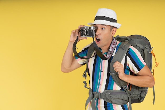 Young backpacker feeling surprised and excited taking a picture with his old camera