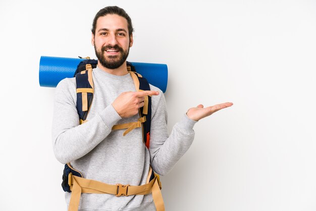 Young backpacker man isolated on a white wall excited holding a copy space on palm.