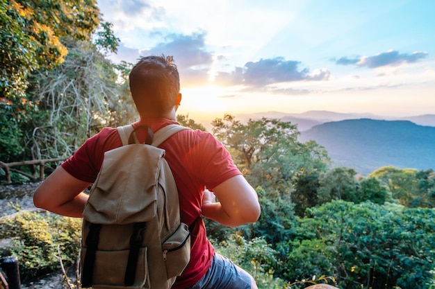 Young backpacker man sitting and looking around on the rocky cliffs in forest with sunset after reach the destination copy space