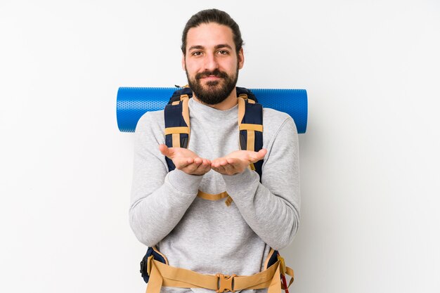 Young backpacker man on a white wall holding something with palms