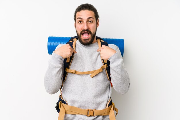 Young backpacker man on a white wall surprised pointing with finger, smiling broadly.