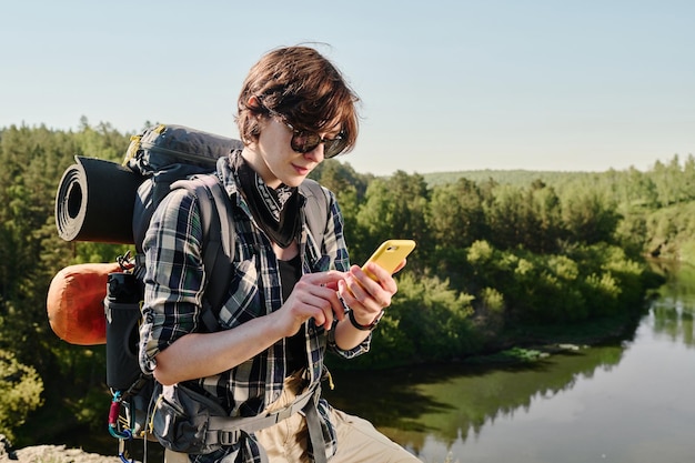Young backpacker texting in smartphone