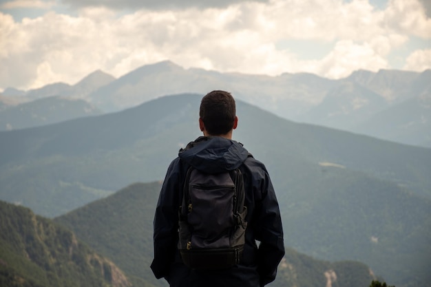 Young backpacker wearing a dark raincoat and enjoying the mountain views