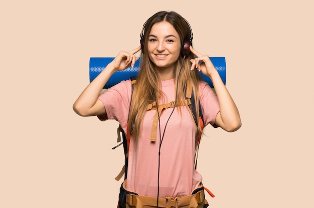 Young backpacker woman listening to music with headphones on yellow wall