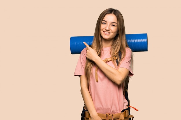 Young backpacker woman pointing to the side to present a product on isolated yellow wall