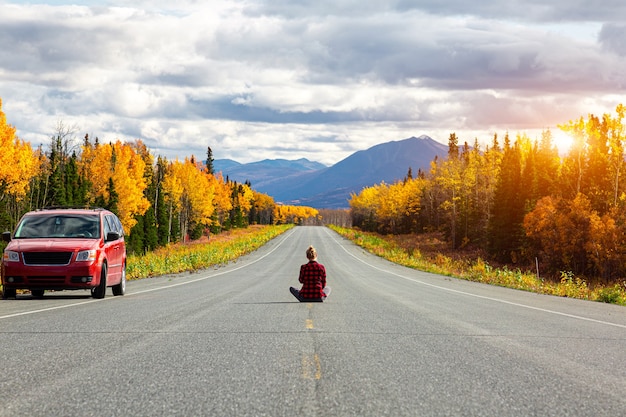 写真 一人で道路に座っているカナダ旅行者の女の子を旅する若いバックパッカーの女性