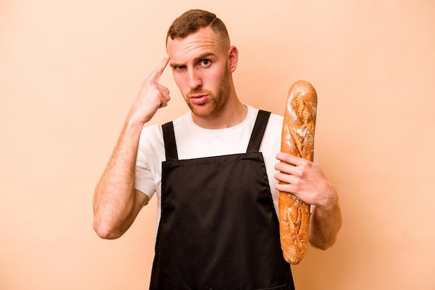 Young baker caucasian man isolated on beige background pointing temple with finger thinking focused on a task