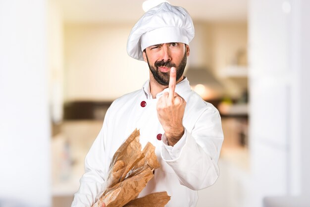 Giovane panettiere in possesso di un po 'di pane e facendo gesto di corno in cucina