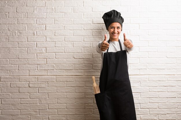 Young baker indian woman against a bricks wall cheerful and excited.