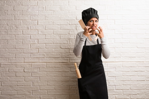 Young baker indian woman against a bricks wall very angry and upset