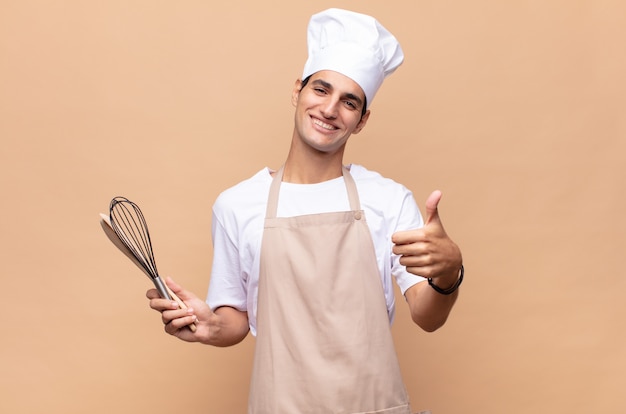 Young baker man feeling proud, carefree, confident and happy, smiling positively with thumbs up