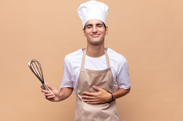 young baker man laughing out loud at some hilarious joke, feeling happy and cheerful, having fun