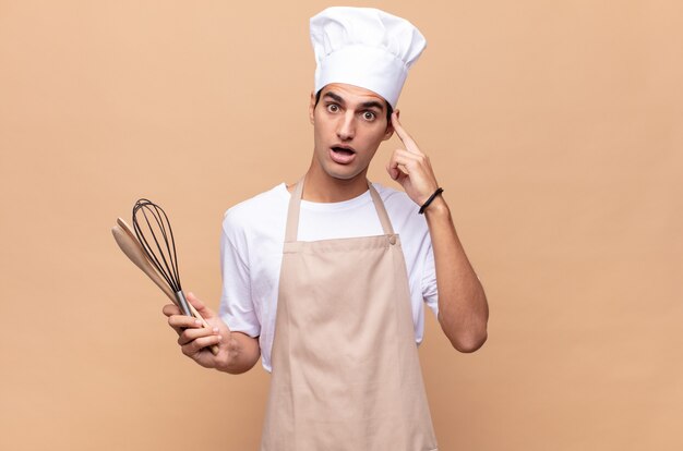 Young baker man looking surprised, open-mouthed, shocked, realizing a new thought, idea or concept