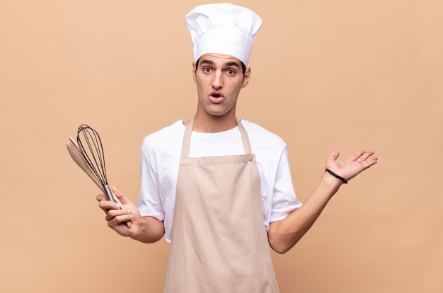 Young baker man looking surprised and shocked