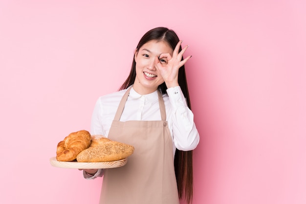 Young baker woman isolated excited keeping ok gesture on eye