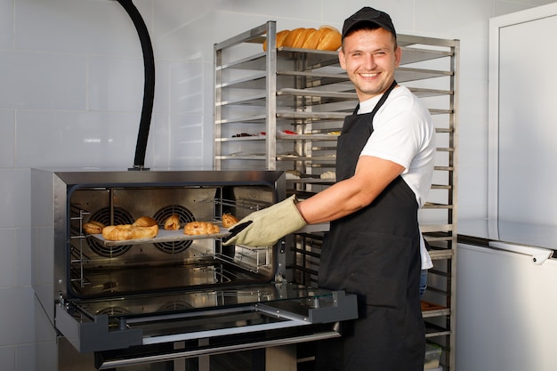 A young baker worker in a bakery is holding pastries
