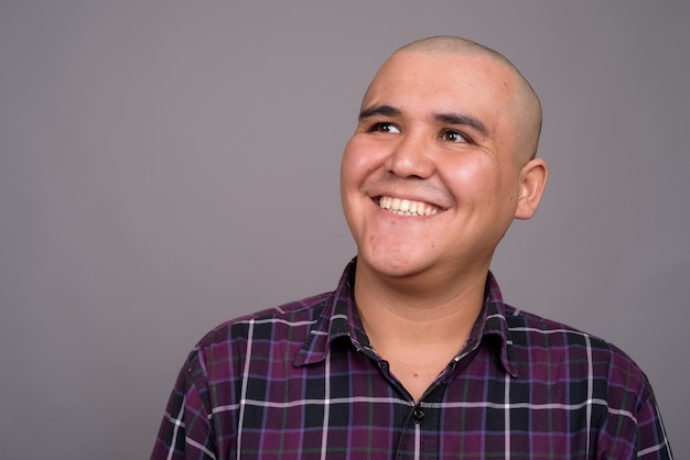 young bald Asian businessman wearing checkered shirt against gray wall