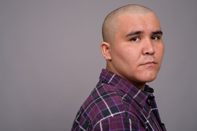 young bald Asian businessman wearing checkered shirt against gray wall