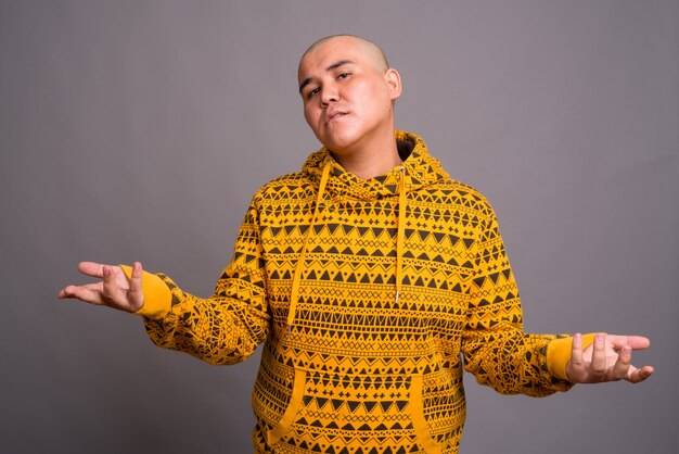 young bald Asian man wearing hoodie against gray wall