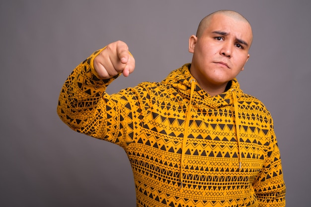 young bald Asian man wearing hoodie against gray wall