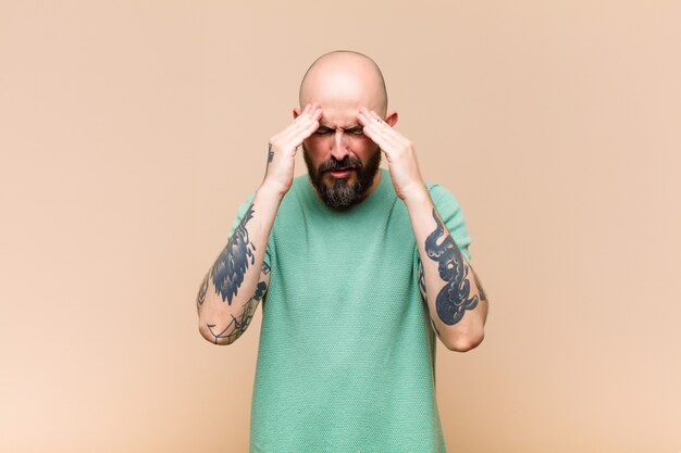 Young bald and bearded man looking stressed and frustrated, working under pressure with a headache and troubled with problems