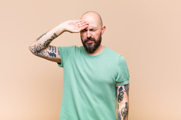 Young bald and bearded man looking stressed, tired and frustrated, drying sweat off forehead, feeling hopeless and exhausted