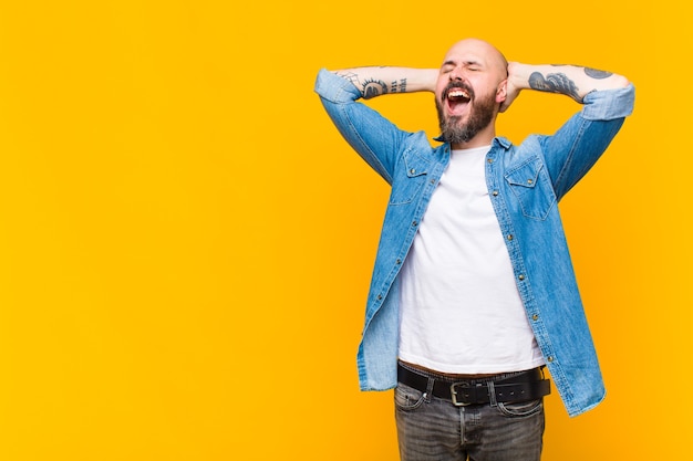 Photo young bald and bearded man smiling and feeling relaxed, satisfied and carefree, laughing positively and chilling