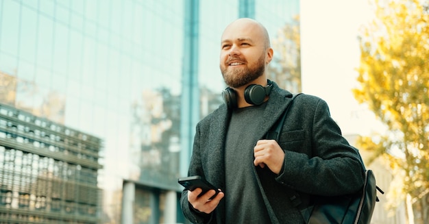 Young bald confident man is walking outdoors wearing backpack and headphones