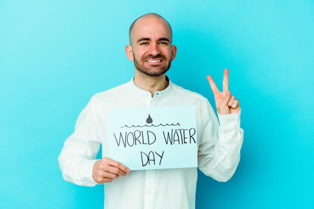 Молодой лысый мужчина празднует всемирный день воды изолирован на синей стене, показывая пальцами номер два