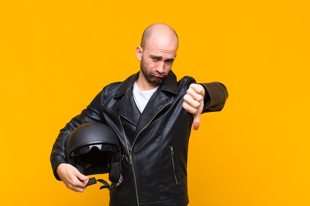 Young bald man feeling cross, angry, annoyed, disappointed or displeased, showing thumbs down with a serious look