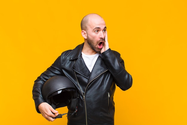 Young bald man feeling happy, excited and surprised, looking to the side with both hands on face