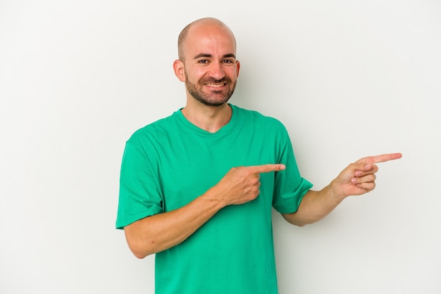 Young bald man isolated on white background excited pointing with forefingers away.