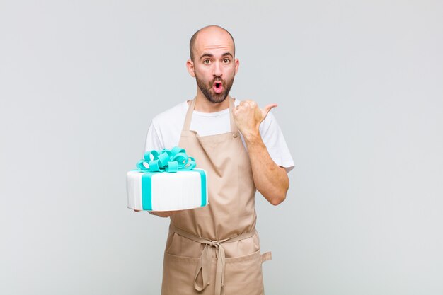 Young bald man looking astonished in disbelief, pointing at object on the side and saying wow, unbelievable