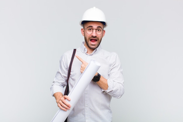 Young bald man looking excited and surprised pointing to the side and upwards to copy space