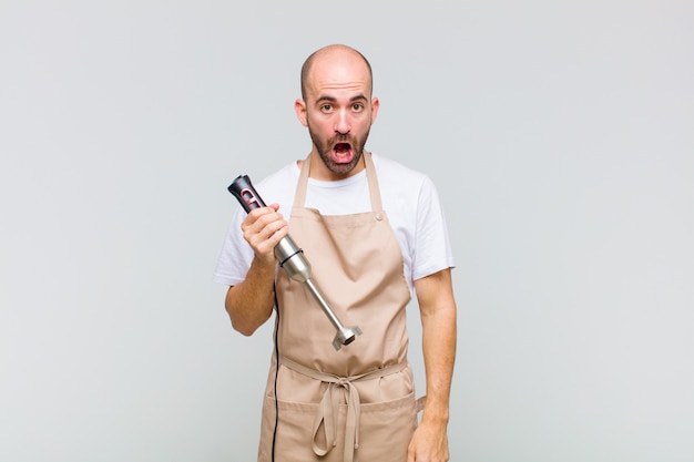 Young bald man looking very shocked or surprised, staring with open mouth saying wow