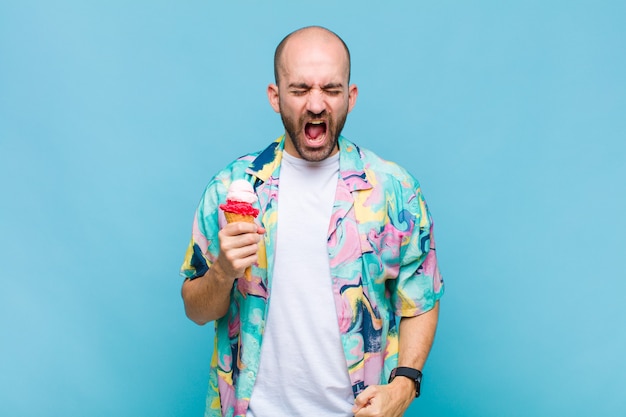 Young bald man shouting aggressively, looking very angry, frustrated, outraged or annoyed, screaming no