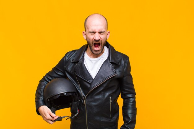 Young bald man shouting aggressively, looking very angry, frustrated, outraged or annoyed