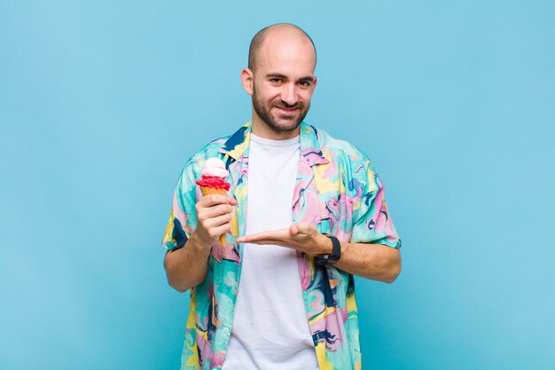 Young bald man smiling cheerfully, feeling happy and showing a concept in copy space with palm of hand