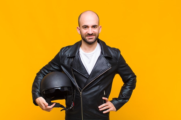 Young bald man smiling happily with a hand on hip and confident, positive, proud and friendly attitude