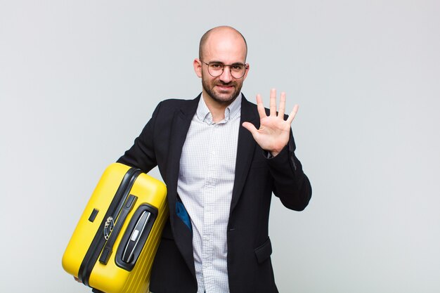 Young bald man smiling and looking friendly, showing number five or fifth with hand forward, counting down