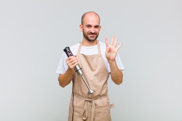 Young bald man smiling and looking friendly, showing number four or fourth with hand forward, counting down