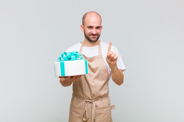 Young bald man smiling and looking friendly showing number one