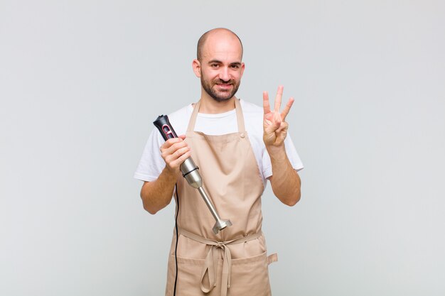 Young bald man smiling and looking friendly, showing number three or third with hand forward, counting down