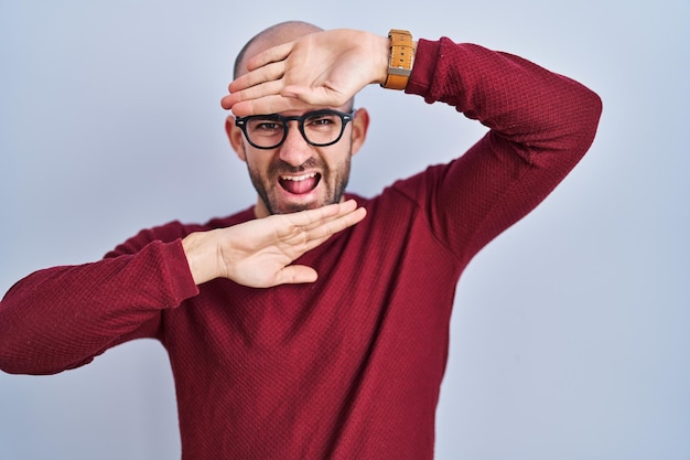 白い背景の上にひげを生やした若い禿げた男が眼鏡をかけ、笑顔で陽気な演奏をし、顔を見せた手でブーイングを覗く。驚いて退場