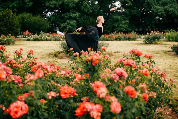 Young ballerina in black dress posing and showing ballet poses in summer park